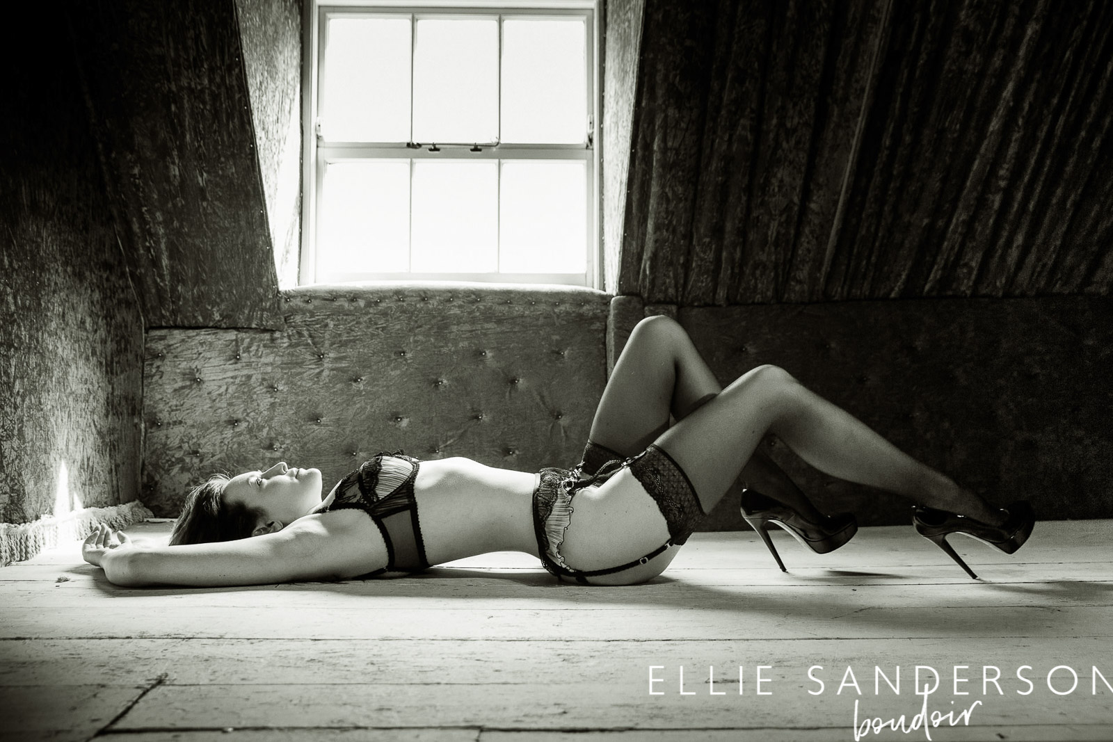 woman lying on a wooden floor posing for a boudoir photo-shoot wearig black lingerie